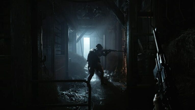 Ein Mann mit Gewehr steht in einem dunklen Raum vor einer lichterhellten Lücke einer Tür, sodass seine Silhoutte zu sehen ist. Darstellung aus dem Spiel Hunt: Showdown.