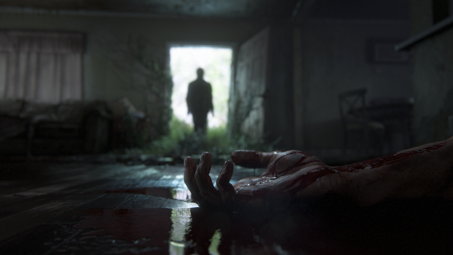 In einer düsteren Hütte steht eine silhouettenhafte Gestalt in der Tür. Im Vordergrund liegt ein blutiger Arm. Die Szene stammt aus dem Spiel The Last of Us: Part II.